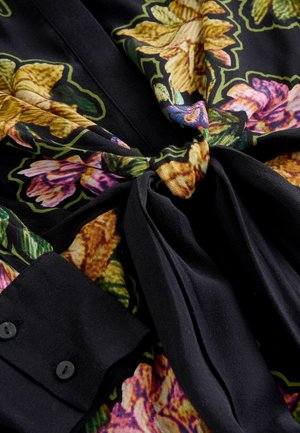 Schwarzer Stoff mit buntem Blumenmuster, das gelbe und rosa Blumen zeigt, gestaltet mit einem gebundenen Taillendetail und einem knöpften Ärmel.