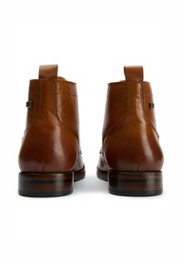 Brown leather ankle boots featuring a seamless design, pull tabs, and a contrasting dark sole with layered accents. Smooth texture, polished finish.