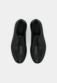 Chaussures en cuir noir présentant une texture lisse, un bout rond et un design traditionnel à lacets. Minimalistes et élégantes avec surpiqûres contrastantes.
