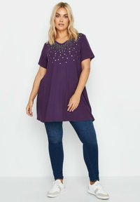 Violetti tunika lyhyillä hihoilla, jossa on helmistä tehty tähtikuvio kaula-aukolla. Yhdistetty tummiin farkkuihin ja valkoisiin tennareihin.