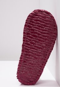 Bordeaux schoenzool met een golvend textuurpatroon, gemaakt van rubber, met een licht glanzende afwerking voor extra visuele diepte.