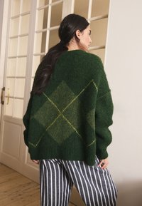 Green knitted sweater with a diamond pattern in lighter green. Paired with navy and white striped pants. Soft texture and oversized fit.