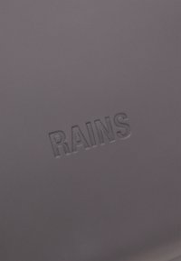 Mørkegrå vanntett produkt med et preget "RAINS"-logo. Overflaten er glatt med en matt finish.