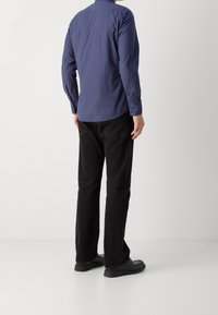 Tmavě modrá dlouhá košile s límcem na knoflíky, spárovan á s černými kalhotami a černými botami. Košile má hladkou texturu a přiléhavý střih.