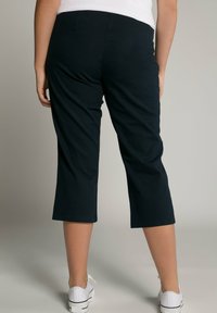 Marineblauwe capri-broeken van een soepele stof, met een rechte snit en een zoom net onder de knie, gecombineerd met witte sneakers.