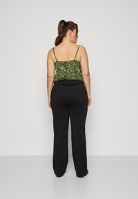 Black wide-leg trousers paired with a green zebra-striped camisole featuring thin straps. The fabric appears smooth with a lightweight design.