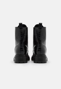 Bottes cheville noires en cuir embossé crocodile avec semelle épaisse, finition texturée et languettes à l'arrière pour un enfilage facile.