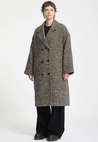 Gray and black houndstooth wool coat with a double-breasted front, oversized fit, wide lapels, and large buttons. Model wearing wide-leg pants.