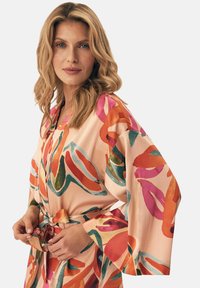 Jedwabny kimono w kolorze brzoskwiniowym z żywymi wzorami botanicznymi w odcieniach zieleni, różu i pomarańczy. Posiada szerokie rękawy oraz zawiązywany pas.