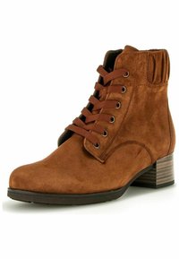 Bottine en suède marron avec un bout rond, un laçage à l'avant et un col élastiqué. Détail de talon en bois texturé ajoutant du contraste.