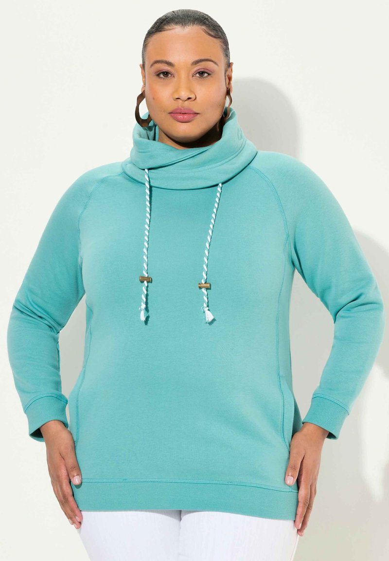 Pullover in pile turchese con collo alto a scialle, lacci bianchi e turchesi, e maniche lunghe. Tessuto morbido e vestibilità rilassata.