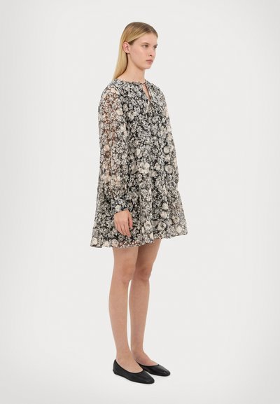 Vestido negro semitransparente con estampado floral, de manga larga, con un escote de botones y cintura fruncida, combinado con bailarinas negras.