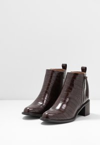 Botines de imitación de cuero marrón con textura de cocodrilo, con cremallera lateral, puntera redonda y un tacón grueso.