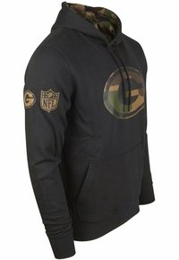 Hoodie noir avec une capuche doublée en camouflage, présentant un grand logo vert et marron et un patch NFL sur la manche, fabriqué en tissu doux.