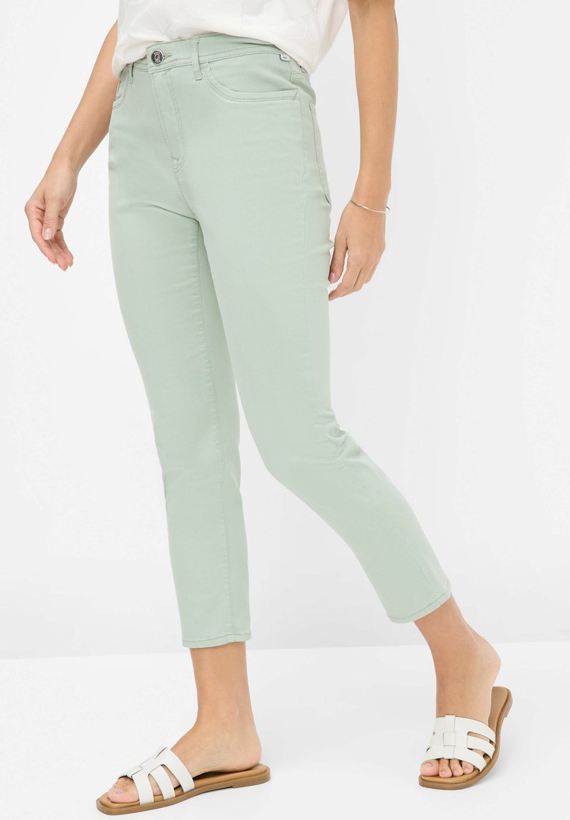 Mintgroene, fitted cropped jeans met een gladde textuur, subtiele voorkantzakken en een knoopsluiting, gecombineerd met witte slidesandalen.