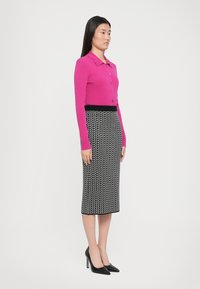 Fuchsia Strickjacke mit Kragen und Knopfverschluss, kombiniert mit einem schwarz-weißen gemusterten Bleistiftrock und schwarzen Stiletto-Heels.