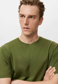 Zelené bavlnené tričko s krátkymi rukávmi a okrúhlym výstrihom. Hladká textúra, priliehavý strih, jednoliate bez vzorov alebo ozdôb.