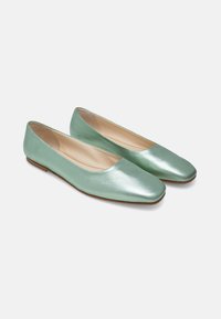 Ballerines vert clair avec une texture lisse et brillante, bout en amande et semelle basse marron. Design simple, sans accessoires ni éléments supplémentaires.