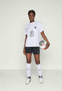 Valkoinen Nike-paita, jossa on violetti logo ja suuri "3"-design, yhdistettynä mustiin shortseihin ja valkoisiin sukkiin, pitelee mustavalkoista jalkapalloa.