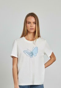 T-shirt bianco in cotone caratterizzato da un grande ricamo di una farfalla blu sul davanti con dettagli intricati. Maniche corte e scollatura rotonda.