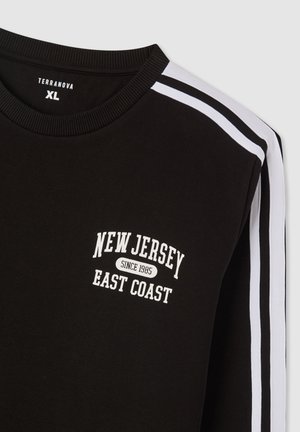 Felpa nera con una grafica bianca che scrive "NEW JERSEY EAST COAST" con "dal 1985" sotto. Strisce bianche sui lati delle maniche.