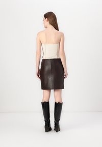 Strapless beige crop top paired with a fitted brown leather mini skirt. Model wearing tall black heeled boots. Back view shown.