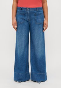 Široke jeans hlače iz jeansa v srednji modri barvi, z sprednjimi in zadnjimi žeponi, klasičnim gumbom in zadrgo ter robom z raztrganimi detajli.