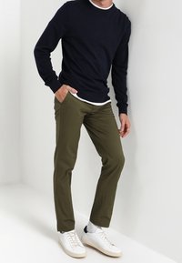 Mörkblå crew-neck tröja, olivgröna byxor och vita sneakers. Släta material, avslappnad passform, med kontrasterande vit innervärdebandskrage.