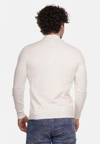 Maglione a maglia color crema con maniche lunghe, design aderente e texture a costine, indossato con jeans in denim, visto da dietro.