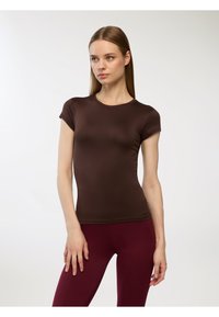 Brązowy dopasowany t-shirt z krótkim rękawem i okrągłym dekoltem, wykonany z gładkiego materiału. W połączeniu z burgundowymi legginsami. Prosty design.