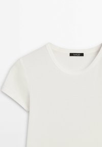 Witte t-shirt met korte mouwen, gemaakt van zachte katoen; heeft een ronde halslijn en een merklabel dat binnenin de kraag is gestikt.