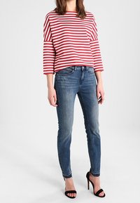 Červený a bílý pruhovaný dlouhý rukáv tričko spárované s modrými slim-fit džíny a černými sandály na vysokém podpatku. Jednoduchý barevný design s jemnou texturou.