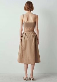 Tan jurk met een aansluitend geribd lijfje en een geplooide rok. Gemaakt van lichtgewicht stof, met dunne bandjes en een verborgen rits aan de achterkant.