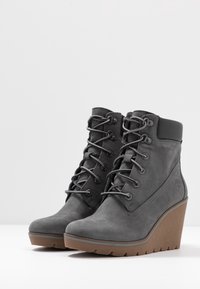 Stivaletti alla caviglia in suede grigio con zeppa, dotati di occhielli in metallo, lacci a contrasto e suola in gomma texturizzata color tan; presenta un emblema con logo sul lato.