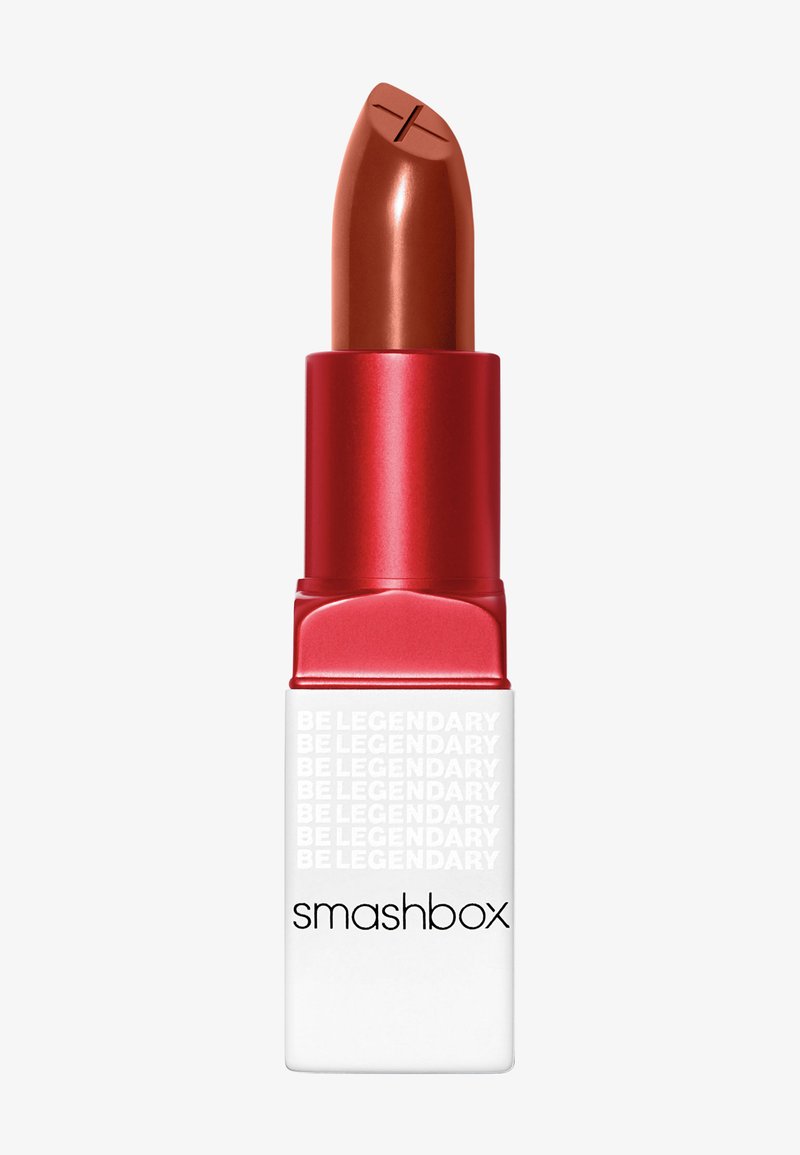 Rouge à lèvres dans un tube métallique rouge avec une base blanche. Le raisin est d'une teinte brune chaude avec une pointe sculptée. Texte "smashbox" sur le corps blanc.