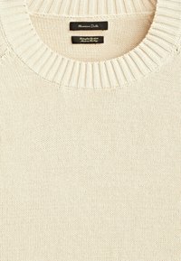 Pull beige en maille avec col rond côtelé et deux étiquettes en tissu noir cousues à l’intérieur de l’encolure.