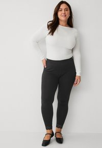 Zwarte leggings met kantaccenten bij de enkels, gecombineerd met een aansluitend wit shirt met lange mouwen. Soepele textuur en rekbare stof.