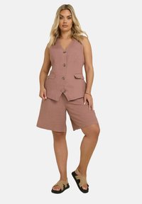 Gilet rosa pallido con cinque bottoni, abbinato a pantaloni corti coordinate di lunghezza al ginocchio. Realizzato in un tessuto testurizzato con due tasche frontali.