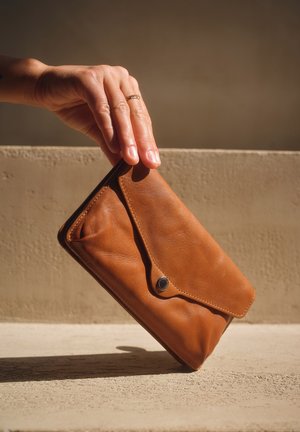 Braune Lederbrieftasche mit Klappenverschluss, glatter Textur und einem silbernen Druckknopf. In einer Hand gehalten, vor einem neutralen Hintergrund positioniert.