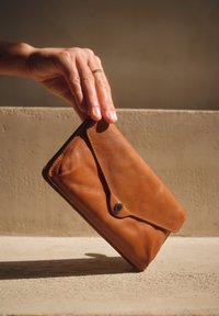 Bruine leren portemonnee met een klep, gladde textuur en een zilveren drukknoop. Valt in de hand, geplaatst tegen een neutrale achtergrond.
