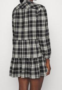 Svart och vit rutmönstrad klänning med långa ärmar, knappstängning med krage, flerlagrad volangkant och mjuk tygkänsla.