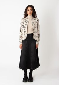 Lillelille mustriga kreemjakker, ribatreeritud kõrge kaelusega top ja must denimist A-line seelik, mille ääres on hõredad servad. Mudel kannab musti sokke ja platvormkingi.