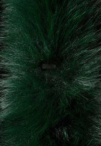 Fausse fourrure verte avec des fibres longues et denses, présentant une base sombre et un éclat subtil. Comprend une petite sangle sombre pour la fixation.