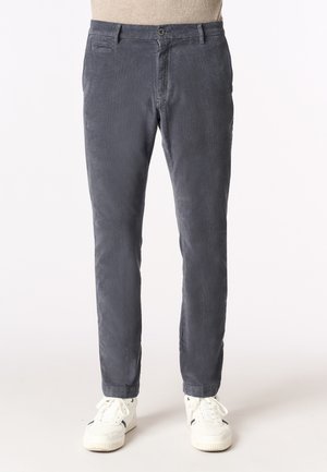 Pantaloni in corduroy grigi con vestibilità slim, dotati di zip, chiusura con bottone, tasche laterali e tessuto texturizzato. Abbinati a sneakers bianche.