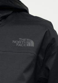 Μαύρο μπουφάν The North Face που δείχνει την περιοχή του επάνω μέρους του στήθους με λογότυπο σε σκούρο γκρι τυπωμένο στην αριστερή πλευρά.