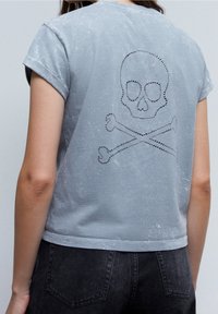 Grå kortærmet t-shirt med en slidstærk struktur. Har et rhinestoneskallede og korsede knogler-design på ryggen.