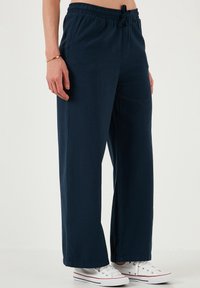 Navyblauwe broek met wijde pijpen, gemaakt van een zachte stof, met een elastische tailleband met trekkoord, zijzakken en een gladde textuur.