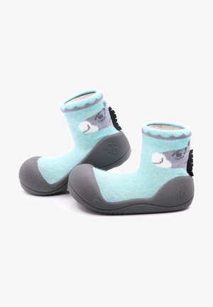 Calcetines de punto de color azul claro, con una suela de goma gris, que cuentan con una cara de animal juguetona y acentos texturizados alrededor del tobillo y la suela.