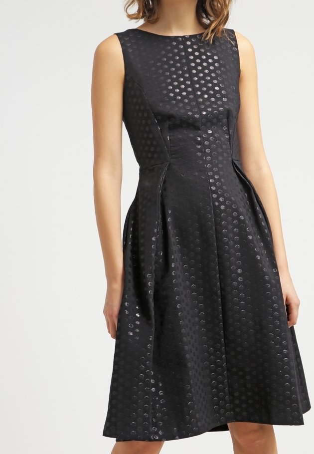 Robe noire sans manches avec un corsage ajusté et une jupe évasée, présentant un motif subtil de pois brillants sur l'ensemble du tissu.