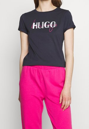 Granatowy t-shirt z krótkim rękawem z białym i różowym logo "HUGO", zestawiony z jasnoróżowymi spodniami dresowymi. Materiał z mieszanki bawełny.